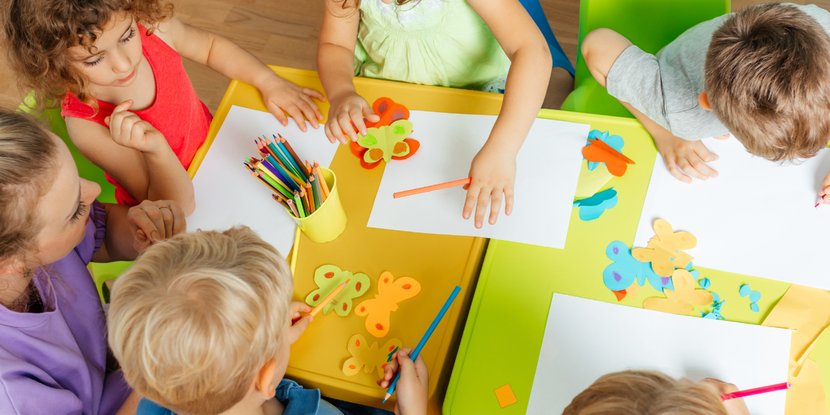 Preschool students sit around a table cutting out pictures of butterflies