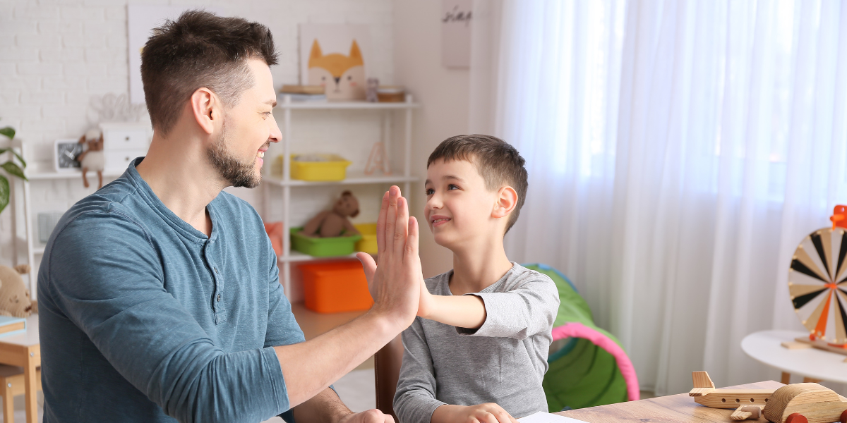 Image of a young boy and his father giving each other a high 5.