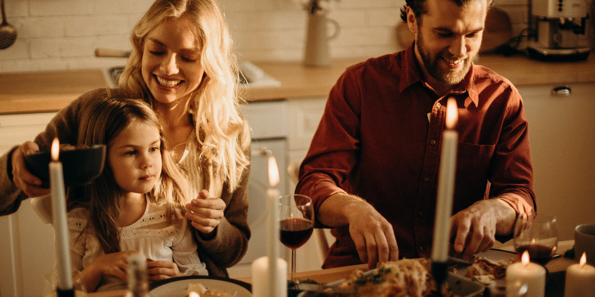 A family consisting of a mom, dad, and young girl eating Thanksgiving dinner