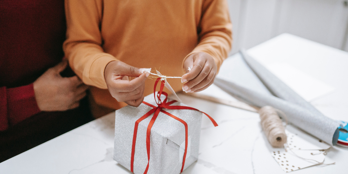 A child wrapping a gift with help from a parent. 