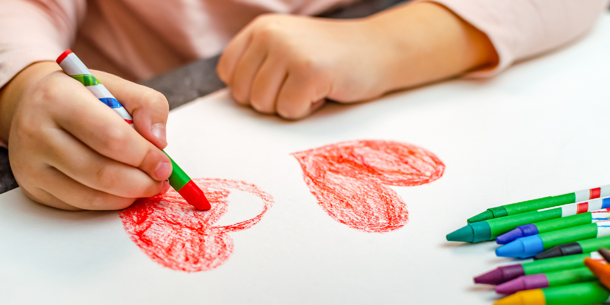 Picture of a preschool female student coloring in a heart shape with a crayon